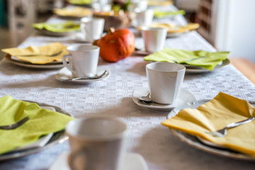Beautiful festive dinner table colorful yellow fall helloween pumpkin decoration coffee mugs saucers plates and spoons