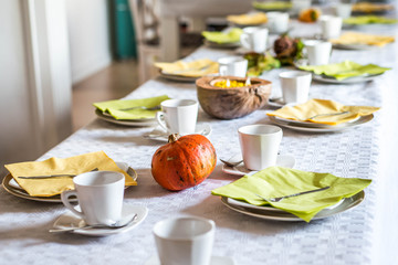 Beautiful festive dinner table colorful yellow fall helloween pumpkin decoration coffee mugs saucers plates and spoons
