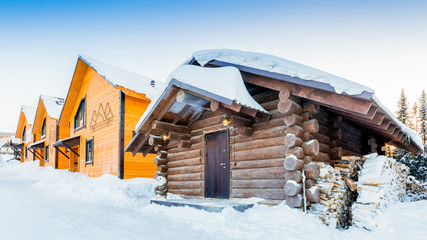 A view of the three wooden houses for guests and the brown bath of their timber in a small village, a ski resort on a winter clear day.