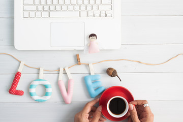 Woman hand holding cup of coffee with love alphabets, Top view on workspace, Valentines Day