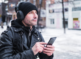 Man looking for a place using GPS map in smartphone. He lost in unknown city. he is dressed in a leather jacket, hat and headphones