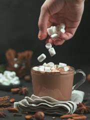 Photo sur Plexiglas Chocolat Marshmallows falls from hand in glass mug with hot chocolate cocoa drink. Copy space. Winter food and drink concept. Flying marshmallow. Dark background. Low key.
