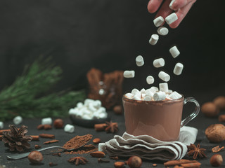 Des guimauves tombent de la main dans une tasse en verre avec une boisson au chocolat chaud et au cacao. Espace de copie. Concept de nourriture et de boisson d& 39 hiver. Guimauve volante. Fond sombre. Discret.