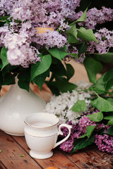 spring garden decorations with blooming lilacs (syringa) bouquet, rustic wooden table and cup of tea