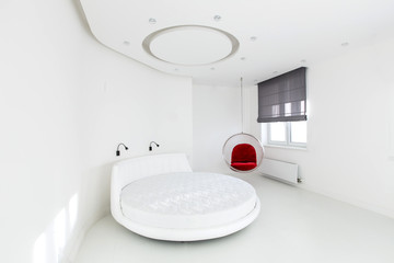 The white bedroom, in which there is a round bed, hangs a red armchair and a window with gray...