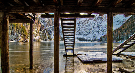 Lake Braies framed by the poles that support the mountain lake boat shelter with blue skies and snow-capped mountains
