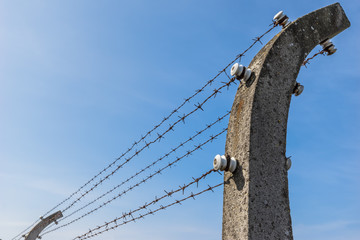 Konzentrationslager KZ / Elektro Stacheldrahtzaun vor blauem Himmel 