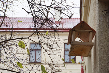 A wooden birdhouse hanging near the wall of a residential building in autumn.
