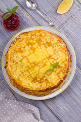 Stack of thin pancakes, crepes on white plate, cup of tea and berry jam, overhead