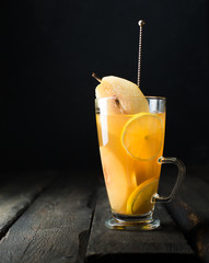Hot spicy festive drink! Mulled white wine with spicy pears, ginger, honey, cinnamon and lemon in a glass with a vintage spoon on a dark wooden background. Winter xmas holidays concept.