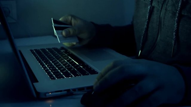 4k closeup footage of hacker holding credit cards typing code on laptop. Man using computer at night. Perfect for cyber crime.