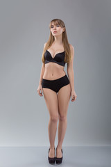 Flawless woman in black bikini on grey background. Photo of girl with slim toned body. Beauty and body care concept