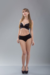 Fototapeta premium Flawless woman in black bikini on grey background. Photo of girl with slim toned body. Beauty and body care concept