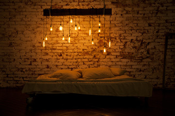 beautiful cozy room in a loft style. bedroom with large bed and white bed linen, and above it the lights are on