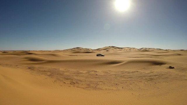 Panorama shot of offroad 4x4 vehicle driving in the sand dunes of Morocco desert - 4K