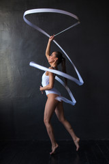 Beautiful woman gymnast with a white ribbon on a black background.