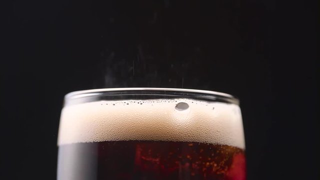 Sizzling white foam in a glass of cola on black background. Close up