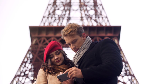 Male and female tourists searching destination in Paris on map in mobile app