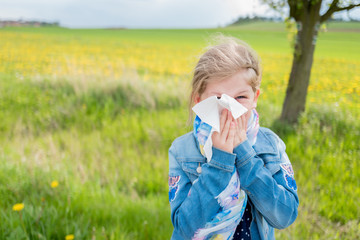 Allergy attack, girl blowing her nose suffering from pollen allergy outdoor in nature