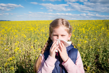 Young girl in nature blowing her nose, suffering from allergy or asthma