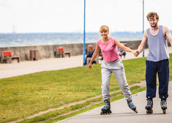 Fototapeta premium Young couple rollerblading in park holding hands.