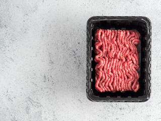 Fresh raw minced beef in plastic tray over light gray cement background with copy space. Top view or flat-lay.