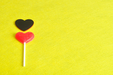 Valentines day. A red heart shape lollipop with a black heart isolated against a yellow background