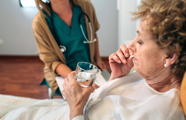 Senior patient taking a pill next to his female doctor - obrazy, fototapety, plakaty