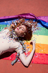 Obraz na płótnie Canvas Chica joven y pelirroja después de una fiesta tumbada sobre una bandera arco iris 