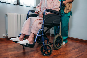 Female doctor carrying elderly female patient in a wheelchair - obrazy, fototapety, plakaty