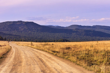 Blue sky. Green Forest. High mountains. Dusty road