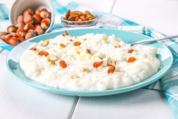 Rice milk porridge with nuts and raisins in a blue dish on a white wooden table.