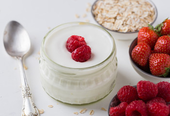 White yogurt in glass bowl with spoon and starwberries on white background.