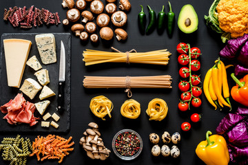 Different fresh ingredients for cooking italian pasta, spaghetti, fettuccine, fusilli and vegetables on a black background. Flat lay, top view.