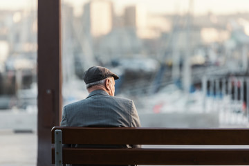 Hombre adulto irreconocible sentado en un banco frente al puerto