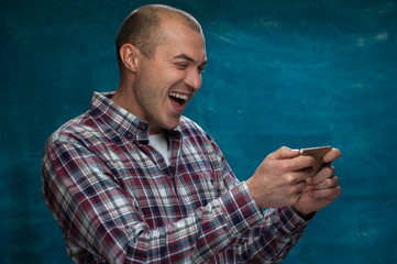 Funny positive man looks into smartphone and laughs at blue  vintage background