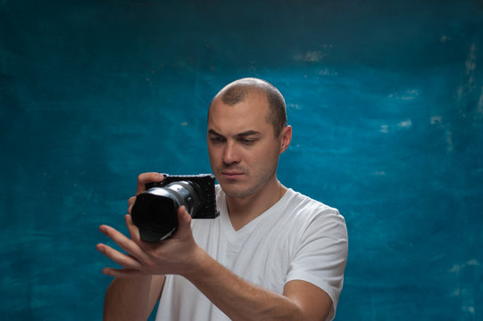 Portrait of serious middle-aged man in white shirt with camera in his hands making photos on blue background. Copyspace