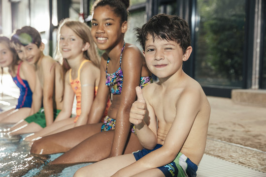 Portrait of smiling children sitting on poolside in indoor swimming pool