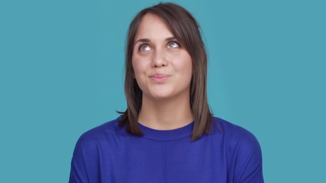 Portrait of woman with brown hair posing on camera with tricky look putting index finger on lips with smile meaning keeping secret isolated on blue background. Concept of emotions