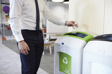 Man in an office throwing plastic bottle into recycling bin - obrazy, fototapety, plakaty