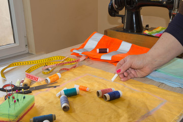 Close up of woman's hands drawing a pattern on yellow tissue. Measuring tape and sewing...