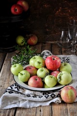 On a wooden table on a cotton towel a metal dish with fresh red and green apples