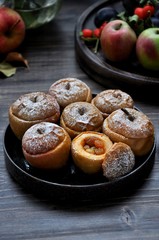 On a wooden table, a dish with baked sweet apples stuffed with raisins and sprinkled with powdered sugar
