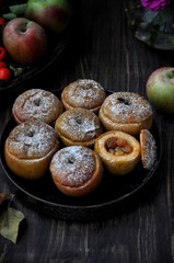 On a wooden table, a dish with baked sweet apples stuffed with raisins and sprinkled with powdered sugar