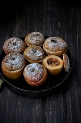On a wooden table, a dish with baked sweet apples stuffed with raisins and sprinkled with powdered sugar. Closeup
