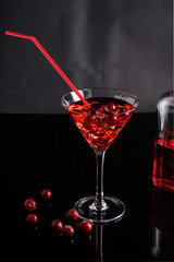 Alcoholic drink of red color in a transparent fougère with ice cubes and cherries on a dark background