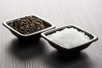 salt and pepper into black bowls on wooden table