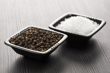 salt and pepper into black bowls, on wooden table