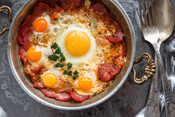 Closeup of Turkish pastirmali and fried egg in a copper pan on wooden table