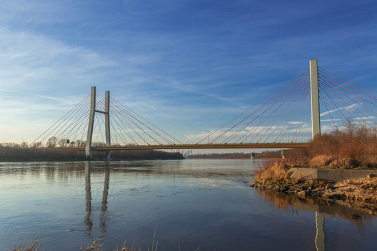 Siekierkowski suspension bridge across the Vistula river with its reflection in water on a sunny day